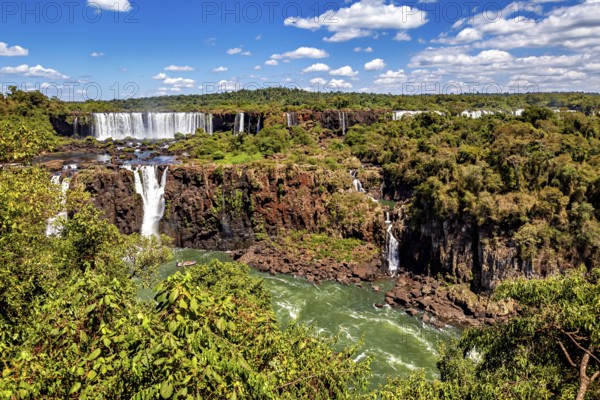 Waterfalls cascade into a river amidst lush vegetation and clear skies, The Iguazu Falls between Argentina and Brazil