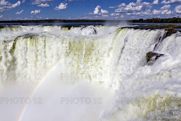 Waterfall with a rainbow over the foaming spray against a cloudy sky, The Iguazu Falls between Argentina and Brazil