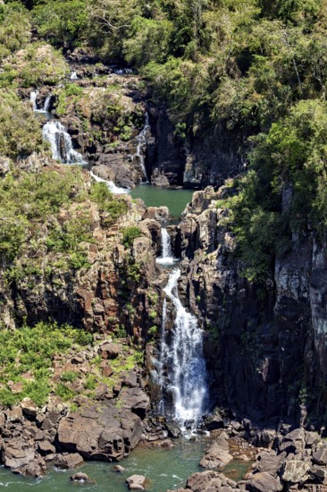 Cascading waterfalls flow over rocks, surrounded by dense vegetation, The Iguazu Falls between Argentina and Brazil