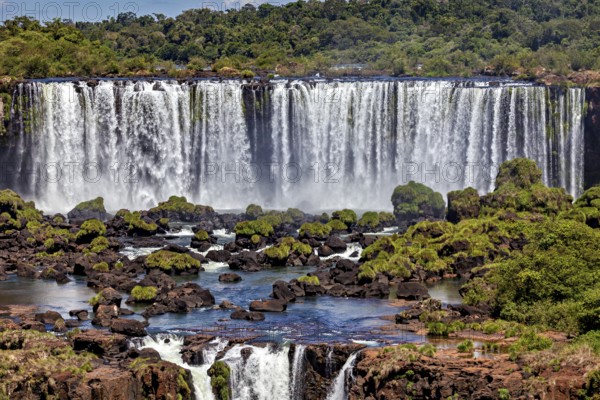 Wide waterfalls cascade over rocks into a river surrounded by lush greenery, The Iguazu Falls between Argentina and Brazil
