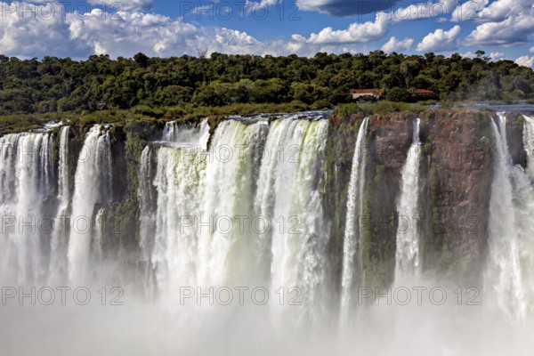 High waterfalls with rocks, spray and forested background under changing skies, The Iguazu Falls between Argentina and Brazil