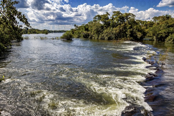 Fast flowing river with rapids surrounded by trees under a cloudy sky, The Iguazu River between Argentina and Brazil