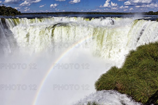 Impressive waterfall with rainbow and spraying spray under a blue sky, The Iguazu Falls between Argentina and Brazil