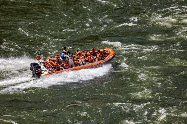 People in an orange-coloured rubber dinghy navigate through turbulent river waters, tourists in a speedboat on the Iguazu River in Argentina