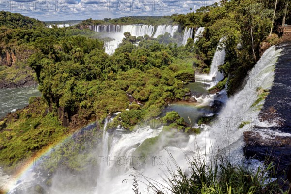 River course with waterfalls and rainbow in a lush forest landscape under a cloudy sky, The waterfalls of the Iguazu between Argentina and Brazil