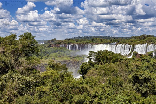 Dense vegetation frames impressive waterfalls under a cloudy sky, The Iguazu Falls between Argentina and Brazil