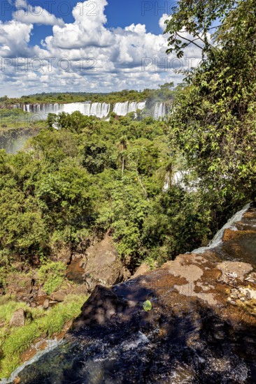 Cliff overlooking impressive waterfalls and thick vegetation against a cloudy sky, The Iguazu Falls between Argentina and Brazil