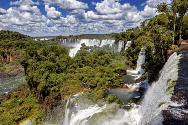 Several magnificent waterfalls and rainbows amidst lush vegetation under clear skies, The Iguazu Falls between Argentina and Brazil