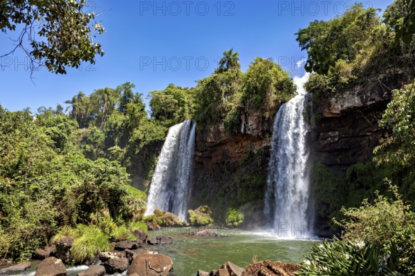 Two waterfalls pouring down amidst dense vegetation and bright sunshine, The Iguazu Falls between Argentina and Brazil