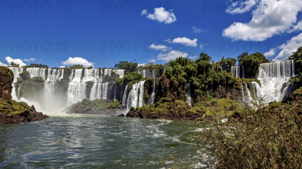 Majestic waterfalls with splashing water surrounded by green vegetation and blue sky, The Iguazu Falls between Argentina and Brazil