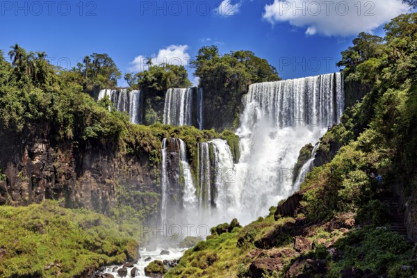 Large waterfalls surrounded by dense vegetation against a blue sky, The Iguazu Falls between Argentina and Brazil