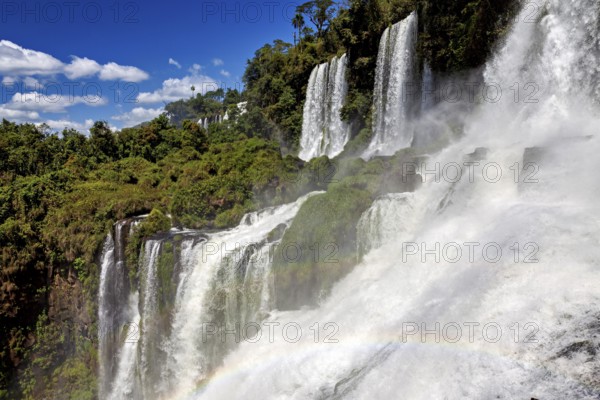 Waterfalls with dense fall and rainbow, embedded in lush forest under a blue sky, The waterfalls of Iguazu between Argentina and Brazil