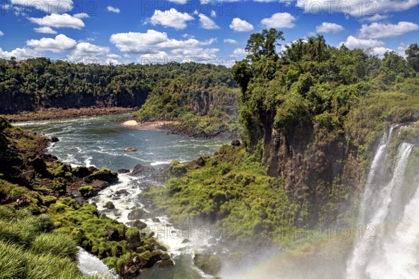 Extensive river landscape with waterfalls and lush riverside vegetation, boat on the water, The Iguazu waterfalls between Argentina and Brazil