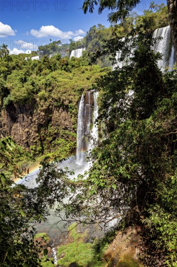 A narrow waterfall plunges through lush greenery and dense vegetation onto stony ground, The Iguazu Falls between Argentina and Brazil
