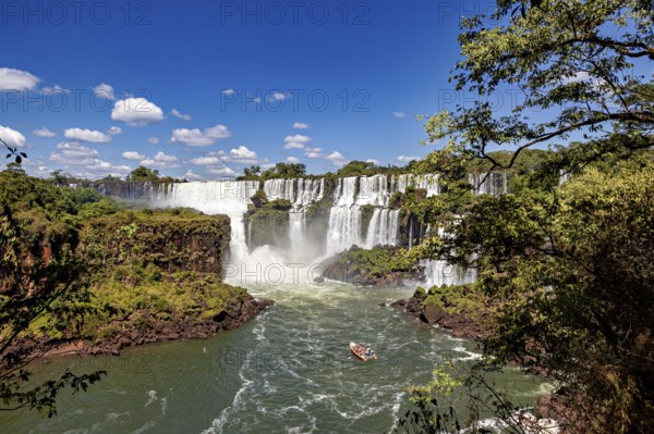 Waterfalls with boat in the river and surrounding jungle under a blue sky, The Iguazu Falls between Argentina and Brazil