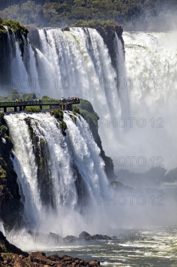 Spectacular waterfall with observation bridge, surrounded by dense vegetation and foaming spray, The Iguazu Falls between Argentina and Brazil
