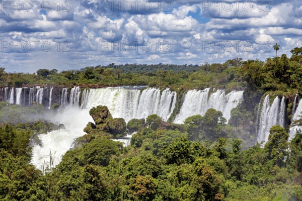 Expansive view of a large waterfall amidst lush green forests and cloudy skies, The Iguazu Falls between Argentina and Brazil