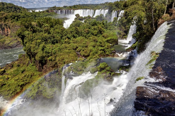 Dramatic waterfall with rainbow and splashing spray amidst dense vegetation, The Iguazu Falls between Argentina and Brazil
