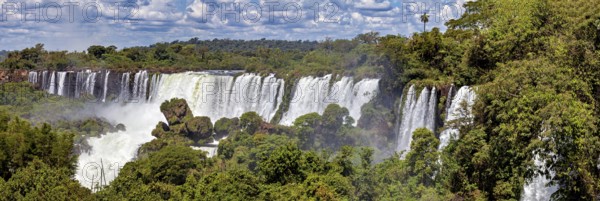 Long waterfall with lush vegetation under a sunny, cloudy sky, The Iguazu Falls between Argentina and Brazil