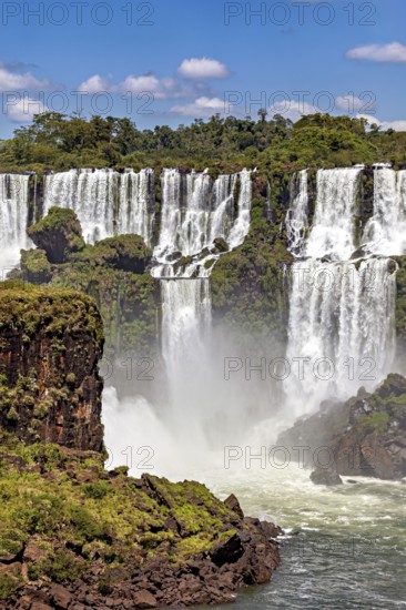 Impressive waterfalls cascade powerfully over rocks, surrounded by green vegetation and under a clear sky, The Iguazu Falls between Argentina and Brazil