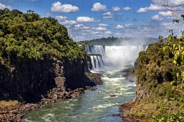 Majestic waterfalls flow between lush vegetation and steep rock faces under a clear sky with white clouds, The Iguazu Falls between Argentina and Brazil