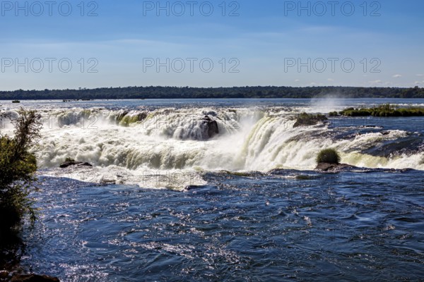 Calm river flows over rapids in bright sunlight, The waterfalls of the Iguazu between Argentina and Brazil