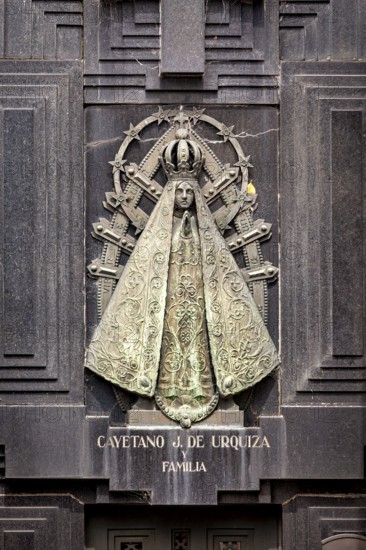 Metal relief of a Madonna on a dark stone surface with engravings and religious symbols, La Recoleta cemetery in Buenos Aires Argentina