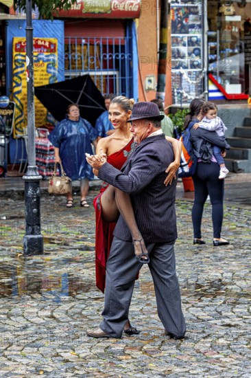 Tango couple in an intimate embrace dancing on a rainy street, surrounded by spectators, The colourful city and tango district La Bocca in Buenos Aires Argentina