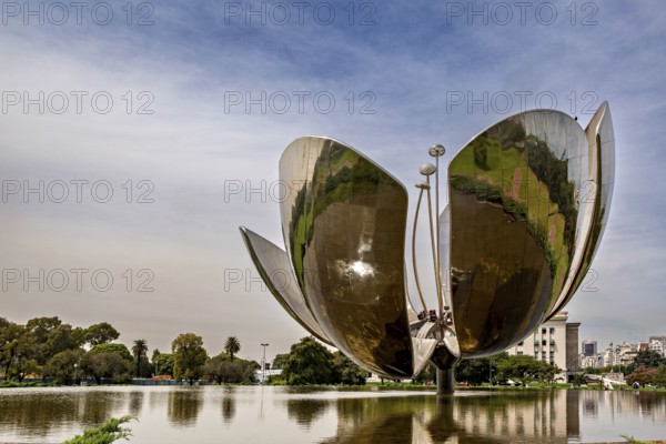 Large metal flower sculpture on the edge of a lake with a cloudy sky in the background, The lotus blossom in Buenos Aires Argentina
