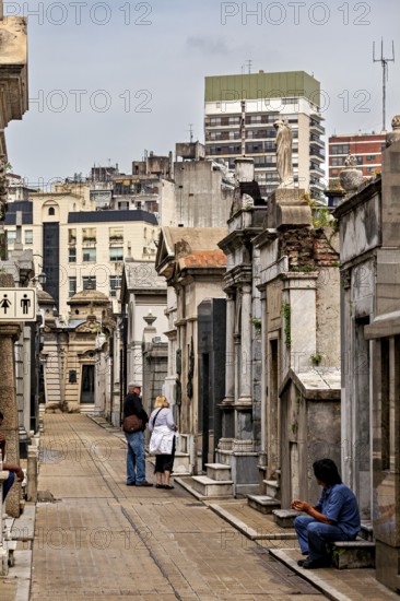 Urban cemetery alley with people and historic graves surrounded by modern architecture, La Recoleta Cemetery in Buenos Aires Argentina
