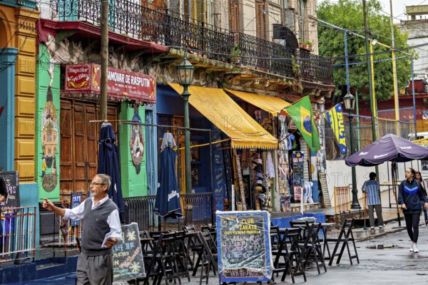 A lively street market with colourful banners and cafés, people stroll past, The colourful city and tango district of La Bocca in Buenos Aires Argentina