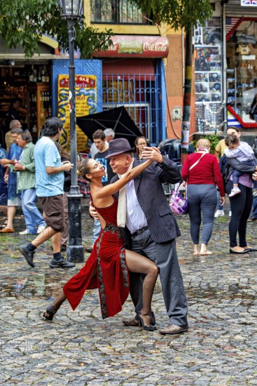 A couple performs impressive tango poses on a rain-soaked street with spectators, The colourful city and tango district of La Bocca in Buenos Aires Argentina