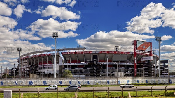 A modern stadium with stands and floodlights under a clear sky and passing cars, the River Plate football stadium in Buenos Aires Argentina