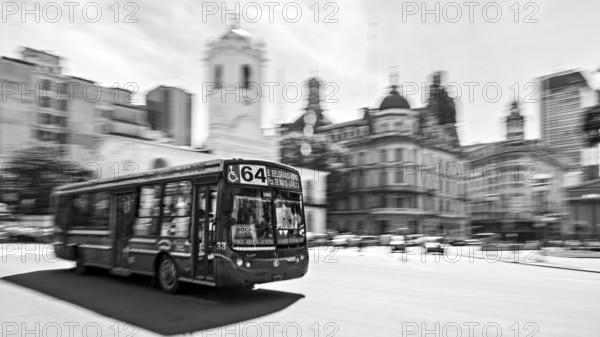 A bus drives through a busy city with historic buildings in the background in black and white, Bus route 64 in the city centre of Buenos Aires in Argentina