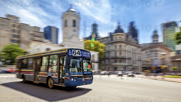A colourful bus drives through a busy city with historic buildings and a blue sky in the background, bus route 64 in the city centre of Buenos Aires in Argentina