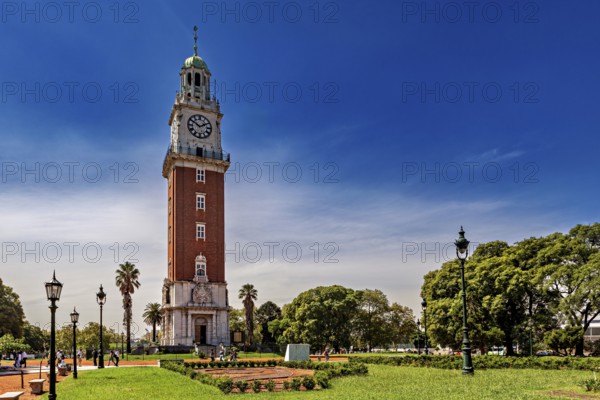A clock tower surrounded by manicured gardens, palm trees and lanterns in a sunny park, The city of Buenos Aires in Argentina