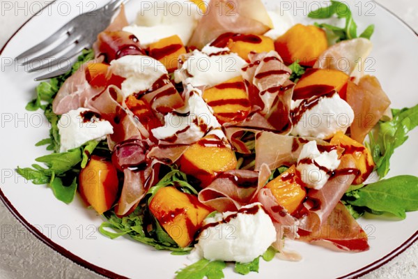 Salad with slices of ripe melon, prosciutto, mozzarella and fresh arugula, decorated with balsamic glaze