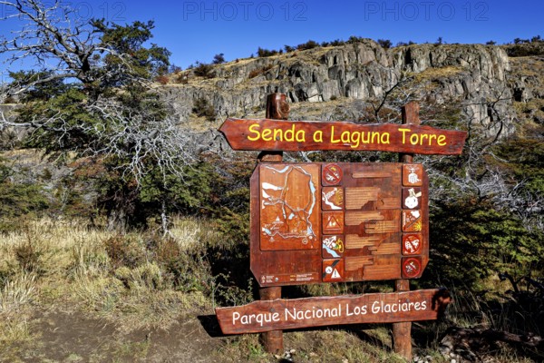 Detailed wooden sign with directions to Laguna Torre in front of a rocky landscape with autumnal colours, The landscape of Patagonia near El Chalten in Argentina