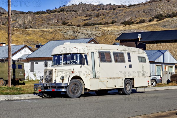 A vintage camper van parked in a mountainous landscape, surrounded by houses and clear skies, A historic Mercedes bus in El Chalten in Patagonia Argentina