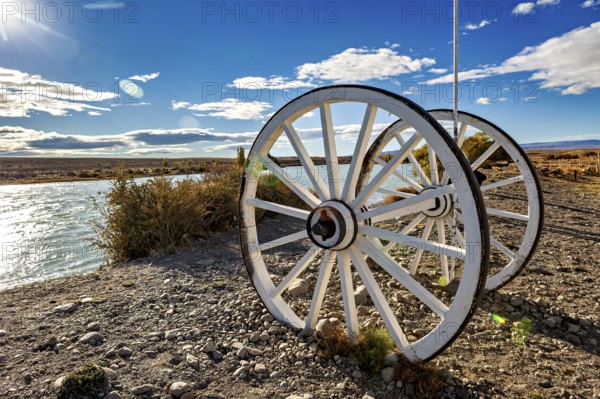 White wagon wheels on the riverbank under a blue sky with clouds, Historic horse-drawn wagon or carriage with wagon wheels in Patagonia