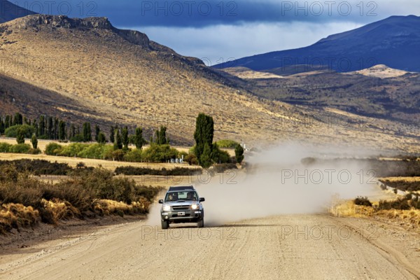 A car drives on a dusty gravel road through a mountainous landscape, Over gravel tracks through Patagonia in Argentina
