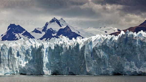 Mighty glacier landscape against a dark sky and snow-capped mountains in the background, The Perito Moreno glacier in Argentina