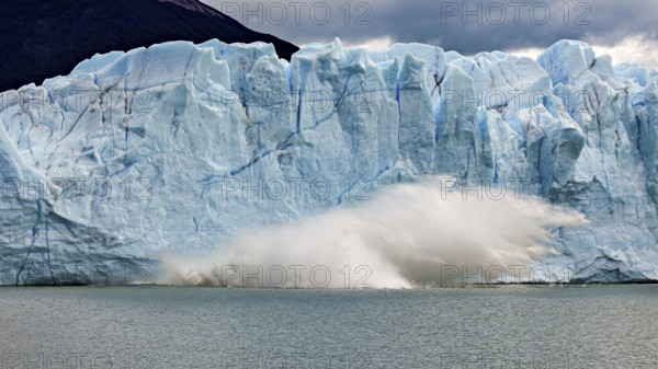 A glacier collapses into the water, blocks of ice tumble down. Threatening clouds add to the dramatic atmosphere, The Perito Moreno glacier in Argentina