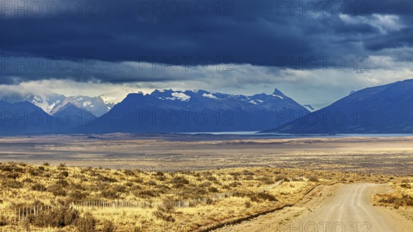 A gravel road leads to a mountain range under a dramatic cloudy sky, The Patagonian landscape near El Chalten in Argentina