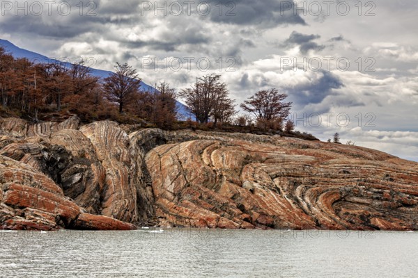 Rough rocks with autumn trees under a cloudy sky by the water, The landscape at Perito Moreno in Patagonia Argentina