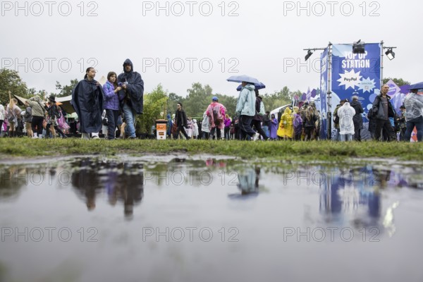 Festival-goers reflected in a puddle at the Lollapalooza Festival in the Olympic Stadium and on the Maifeld, Berlin, 12 July 2025