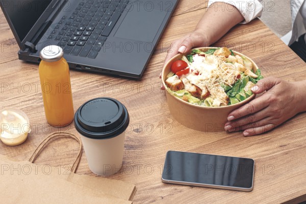 A woman is working on a laptop at home, there is food on the table, salad, coffee and juice, delivery, work at home