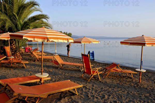 Beach, deckchairs, sunshades at the lido, Lake Bolsena, Lago di Bolsena, volcanic crater lake, calm smooth water surface, warm evening light, Bolsena, Province of Viterbo, Lazio, Italy