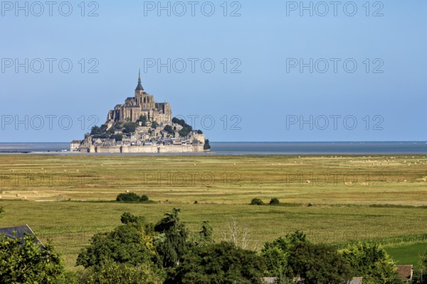 Historic abbey on a rocky island off the coast of France, surrounded by green fields and blue skies, Mont Saint Michel in Normandy, France