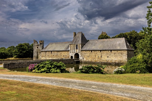Historic castle with moat and garden under a dramatic sky, Gratot Castle in Normandy, France